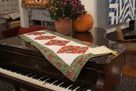 red and green quilted holiday table runner displayed on top of piano