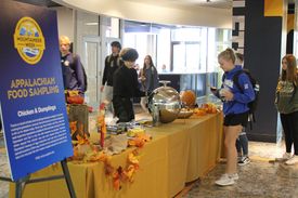 A student gets a food sample from a table in the Mountainlair commons area