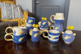 Ceramic mugs decorated in whimsical golds and blues and featuring the state of West Virginia