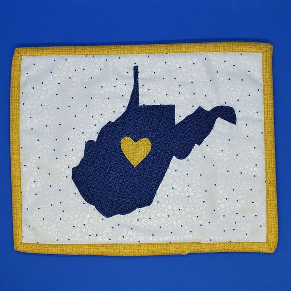 quilted mug rug with a blue applique in the shape of the State of West Virginia and a gold heart. 