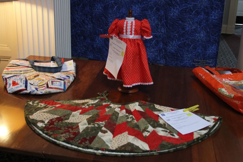 Quilted doll dress, tree skirt, bag on display table during 2019 Quilt Show